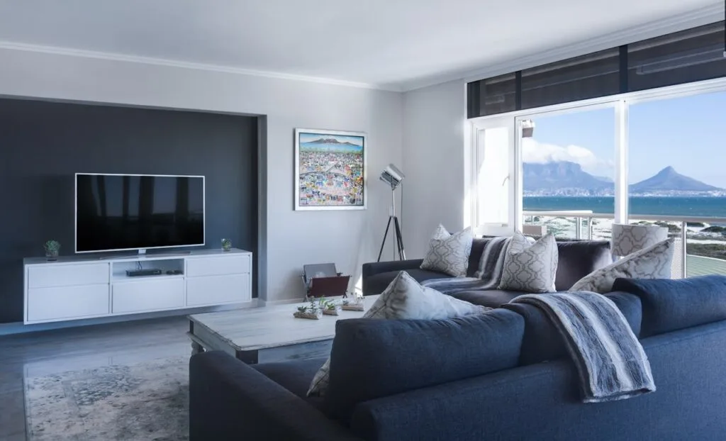 A bright modern living room with large windows, ocean views, and a cozy gray sectional sofa arranged around a minimalist coffee table.