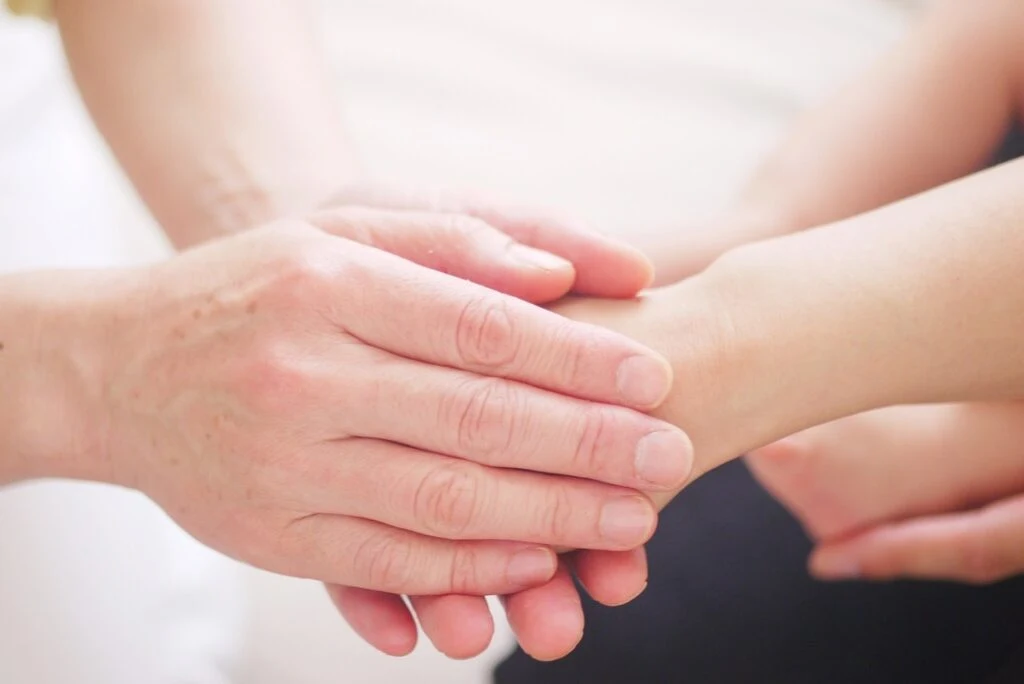 A therapist holding a patient&rsquo;s wrist with both hands, providing gentle support and physical care during recovery.