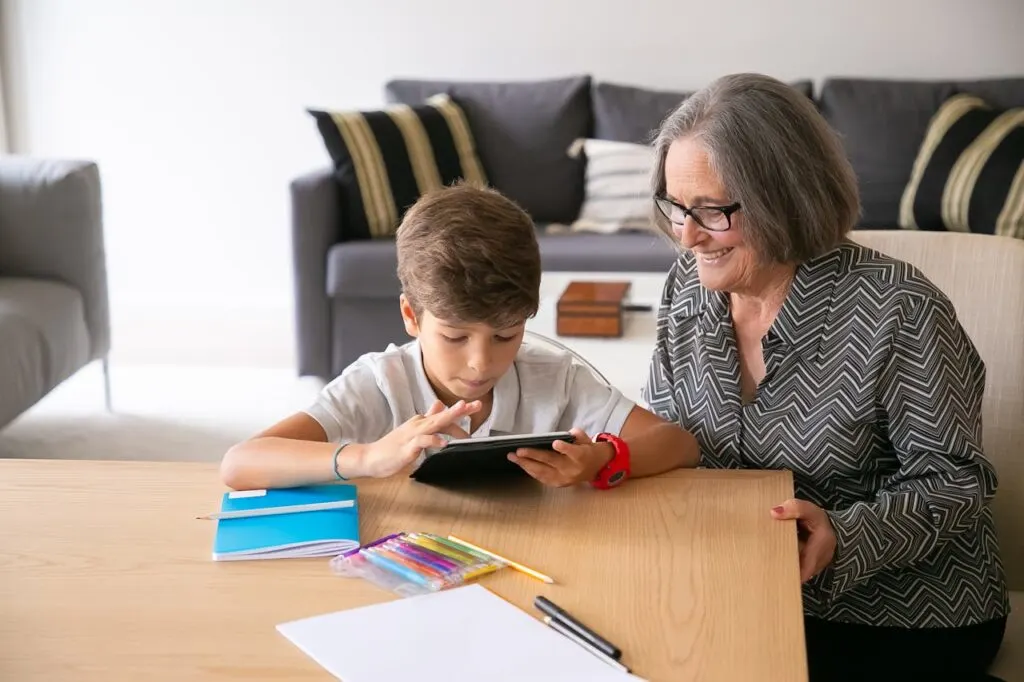 Grandparent smiling while spending quality time with a child using a tablet at home, highlighting connection and family support across generations.