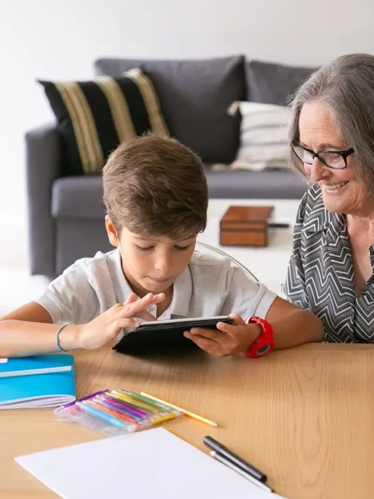 Grandparent smiling while spending quality time with a child using a tablet at home, highlighting connection and family support across generations.