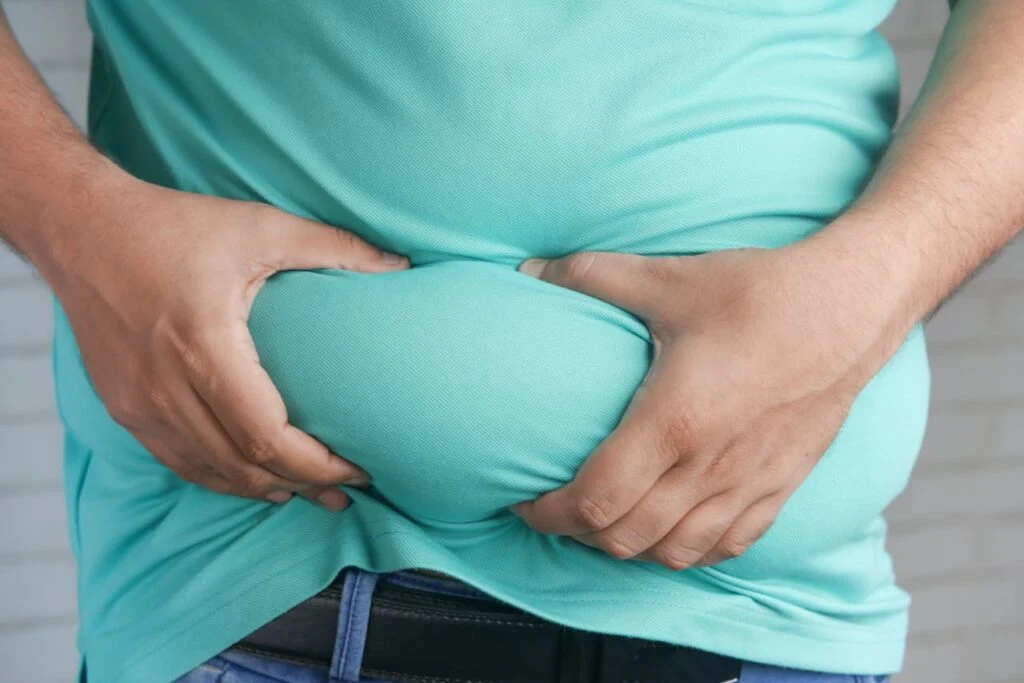 Person holding excess belly fat, illustrating the challenges that lead many people to choose specialized weight loss foods for long term support.