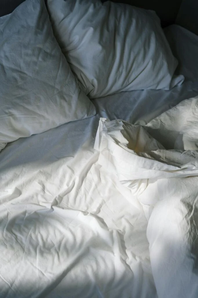 Soft white pillows and wrinkled sheets on a sunlit bed, showing the relaxed look of year round bedding.