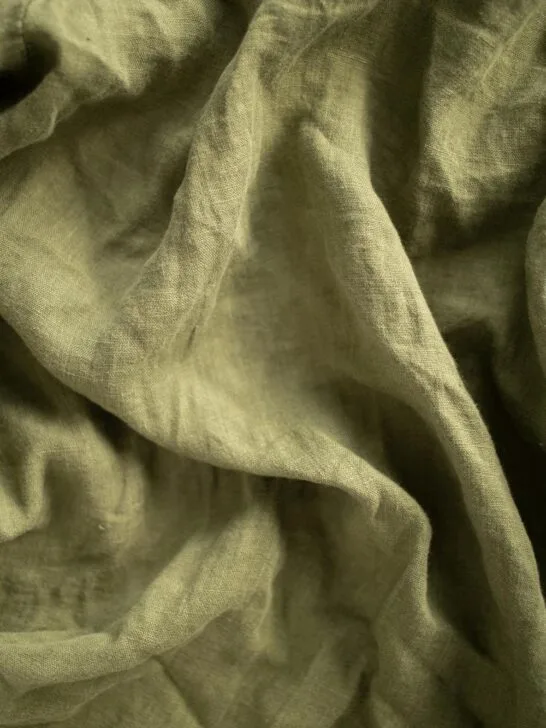 Close-up view of softly wrinkled green fabric, highlighting natural texture, breathability, and a relaxed woven finish.