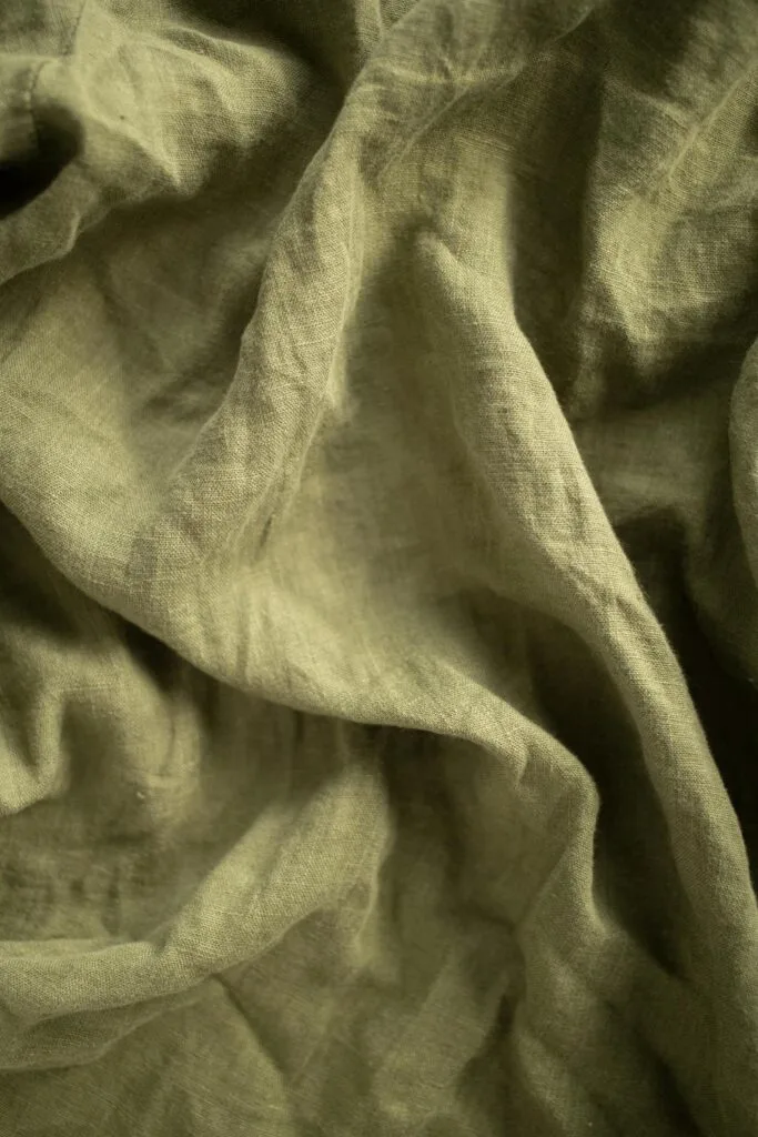 Close-up view of softly wrinkled green fabric, highlighting natural texture, breathability, and a relaxed woven finish.