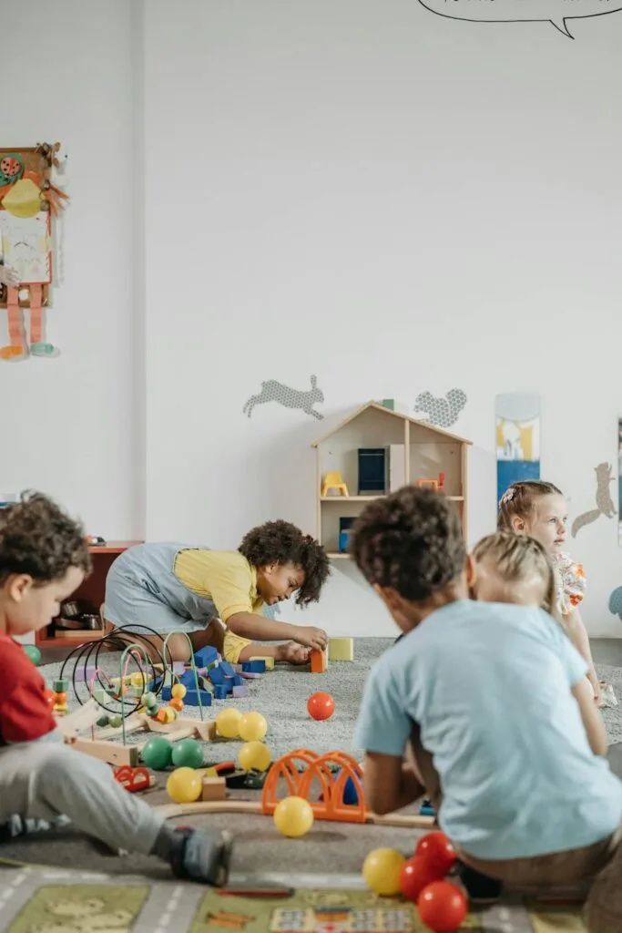 Young children playing together on the floor with educational toys in a bright daycare classroom setting.