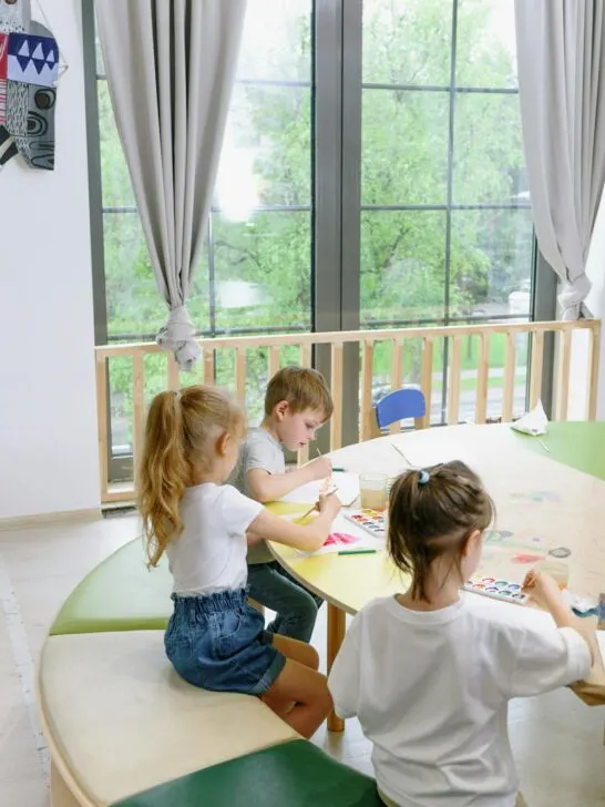 Children painting and creating artwork at a table in a daycare classroom, supporting academic confidence in children through hands-on learning.