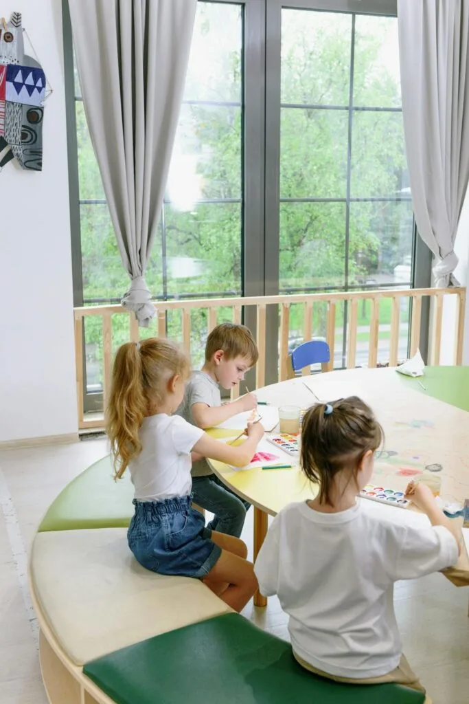 Children painting and creating artwork at a table in a daycare classroom, supporting academic confidence in children through hands-on learning.