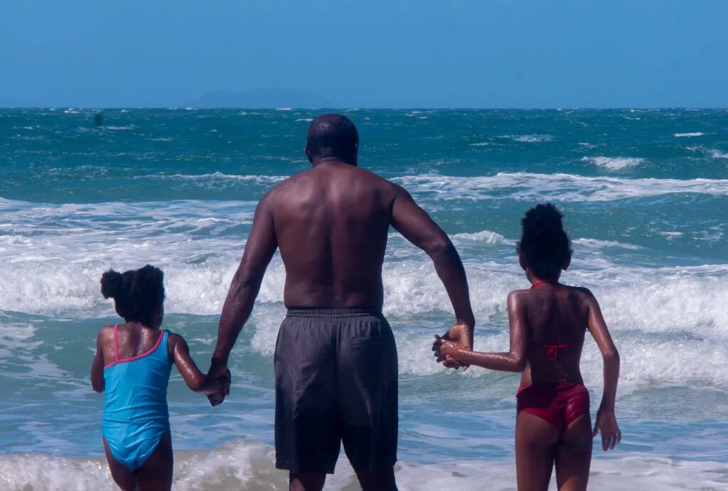 Family travel budget planning starts with simple outdoor days, like a parent holding hands with children walking along the beach.