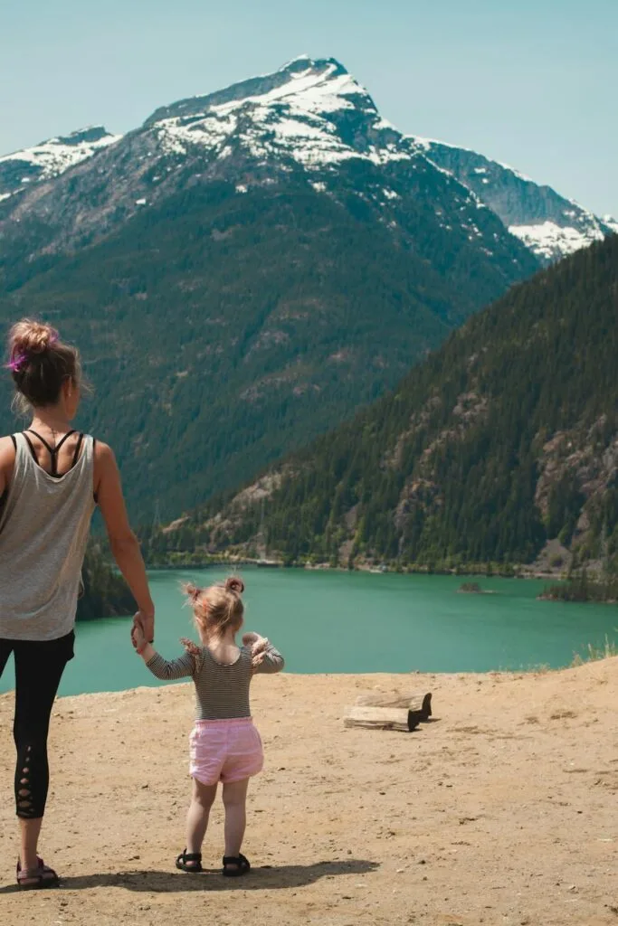 A parent and young child holding hands while overlooking a mountain lake during a family outdoor adventure.