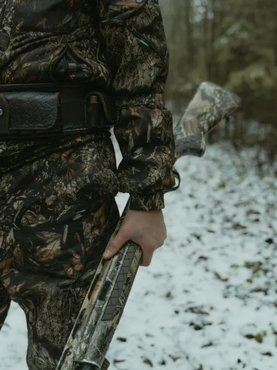 A hunter holding a firearm while wearing camouflage clothing, representing hunting skills you can practice at home to build confidence and control.