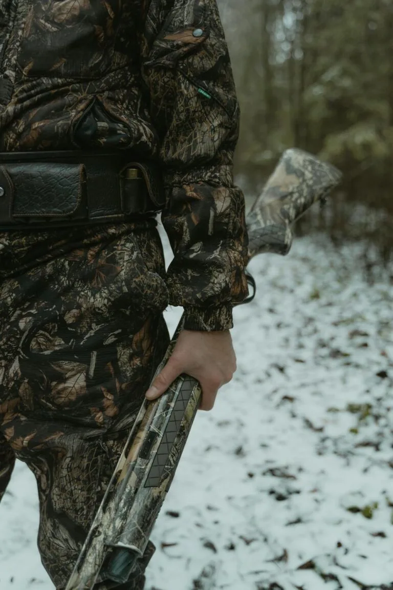A hunter holding a firearm while wearing camouflage clothing, representing hunting skills you can practice at home to build confidence and control.