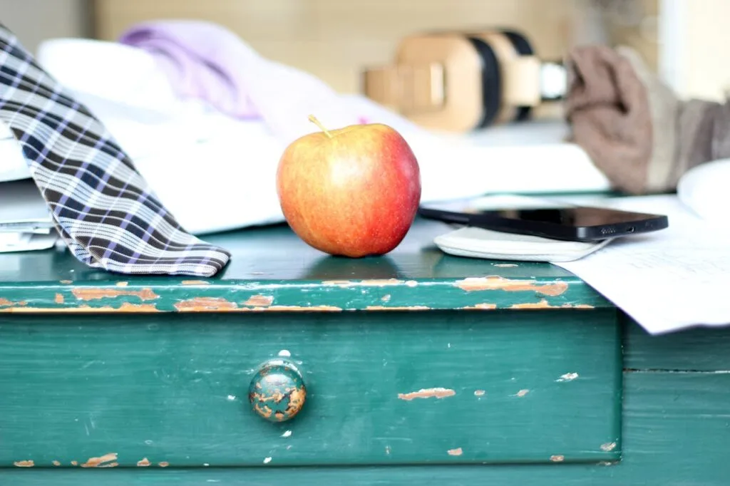 Worn green painted wooden drawer with chipped paint, a red apple on top, and everyday items resting on the surface, showing signs of age and use.