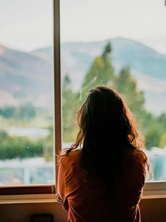 Woman standing by a window in quiet reflection, symbolizing emotional changes and self-awareness during menopause