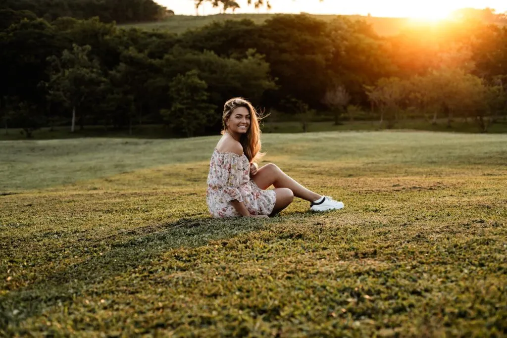 Woman sitting on grass at sunset wearing a floral mini dress, a relaxed and comfortable look for mini dresses for family gatherings.