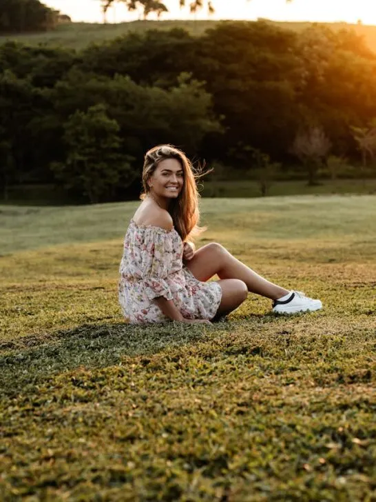 Woman sitting on grass at sunset wearing a floral mini dress, a relaxed and comfortable look for mini dresses for family gatherings.