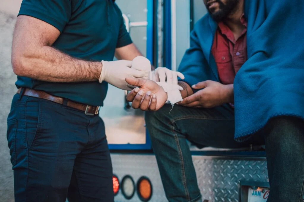 A paramedic provides first aid to an injured man seated on an emergency vehicle after a traffic accident.