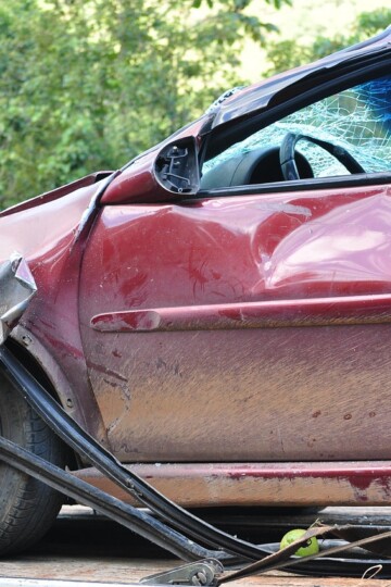 Close view of a red car with severe rear side damage and deployed airbag during an accident reconstruction investigation documenting impact forces