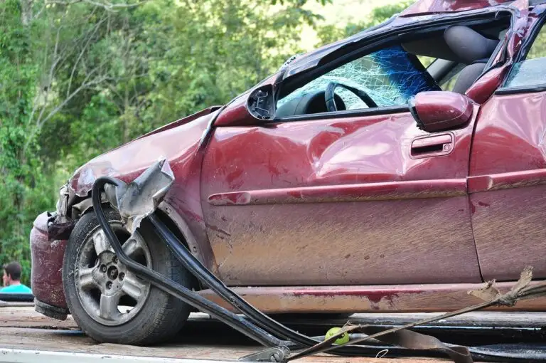 Close view of a red car with severe rear side damage and deployed airbag during an accident reconstruction investigation documenting impact forces