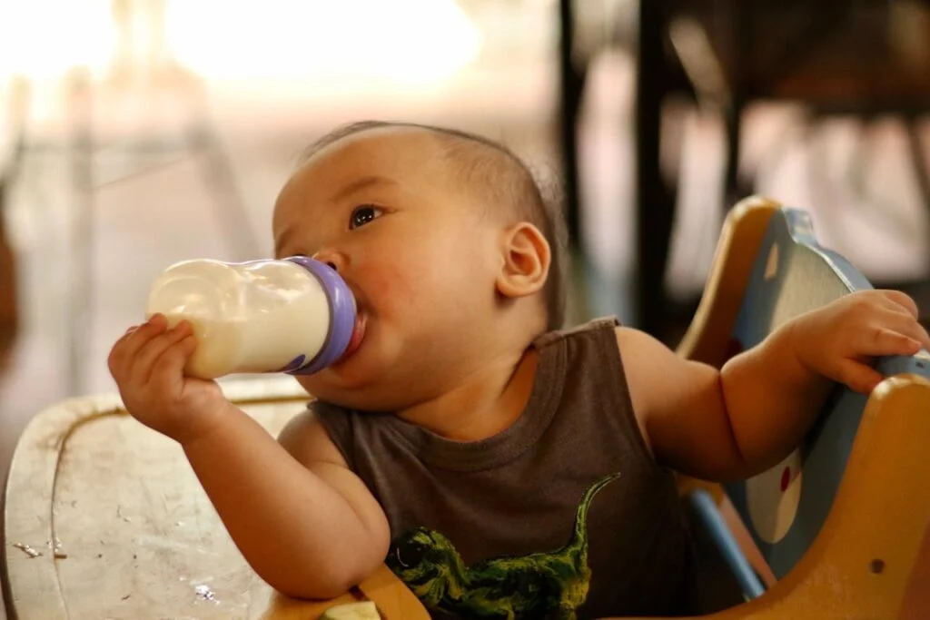 Baby drinking milk from a bottle while sitting in a high chair, supporting healthy growth and early feeding milestones