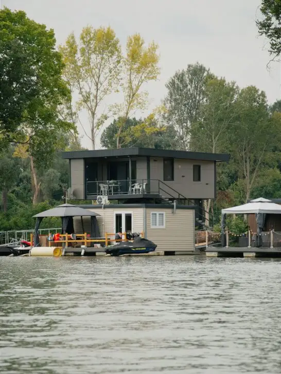 Modern floating home showcasing boathouse living benefits with private dock, upper deck seating, and jet ski on calm waterfront
