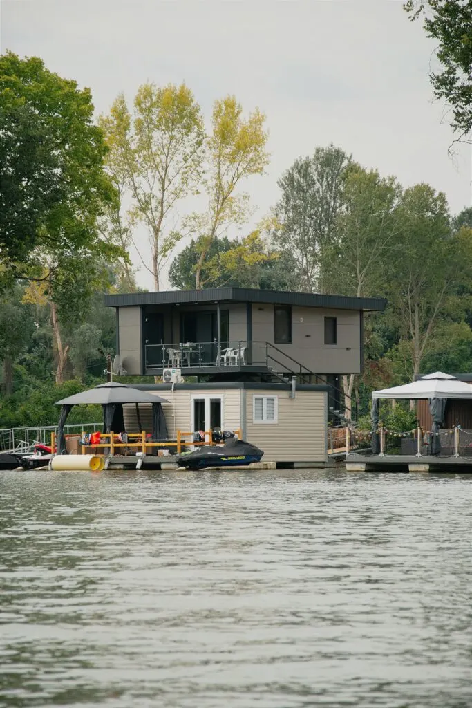 Modern floating home showcasing boathouse living benefits with private dock, upper deck seating, and jet ski on calm waterfront