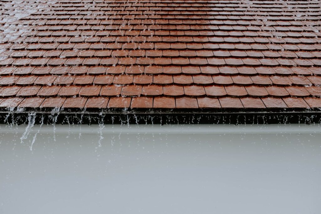 Rainwater overflowing from roof edge without proper gutter system, showing risk of water damage to home exterior