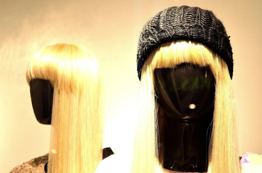 Two mannequin heads displaying sleek blonde wigs, one styled with a knit beanie, showcasing low-maintenance wigs for moms that offer effortless everyday style.