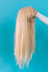 Long straight blonde wig being held up against a bright blue background, highlighting smooth texture and natural-looking shine.