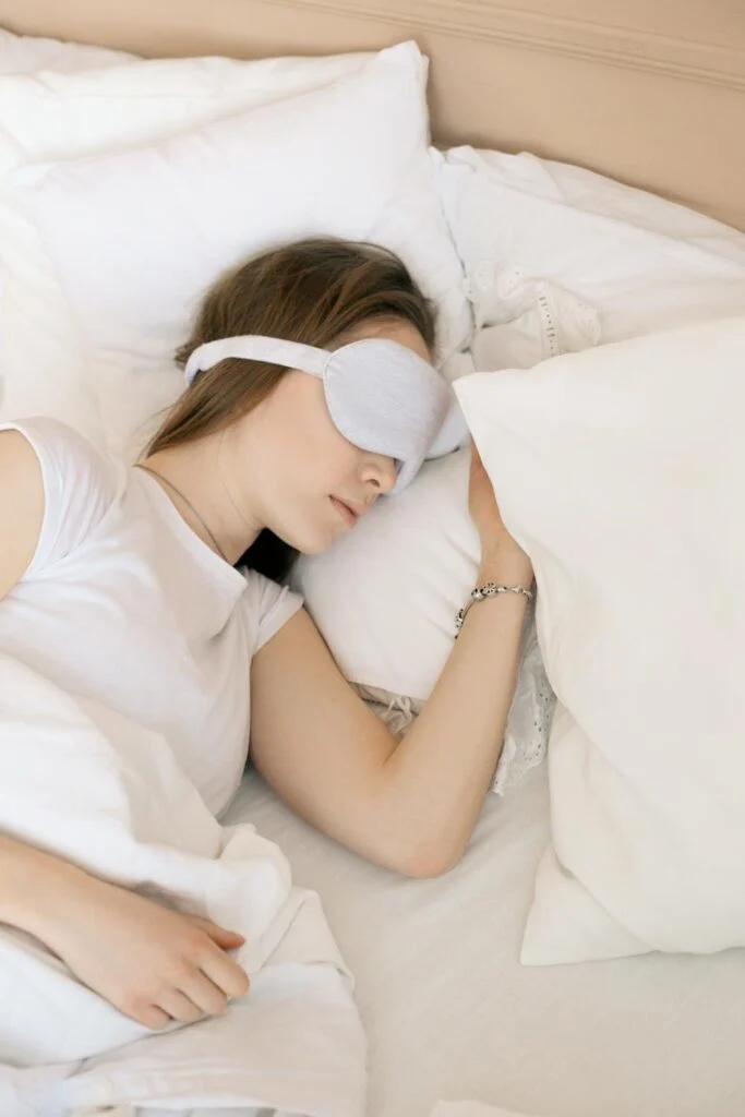 Woman resting peacefully in white bedding and eye mask, demonstrating quality bedding for better sleep