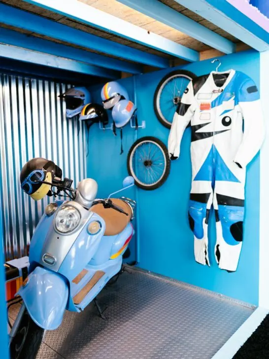Organized garage space with helmets, bike wheels, riding suit, and scooter neatly stored on walls and hooks