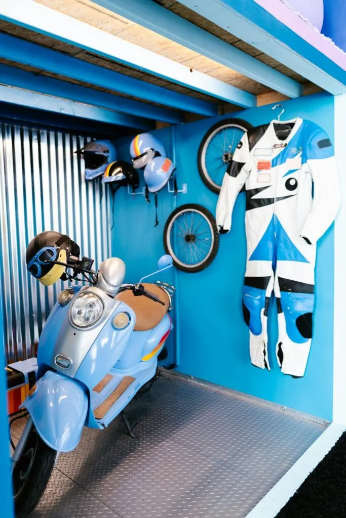 Organized garage space with helmets, bike wheels, riding suit, and scooter neatly stored on walls and hooks