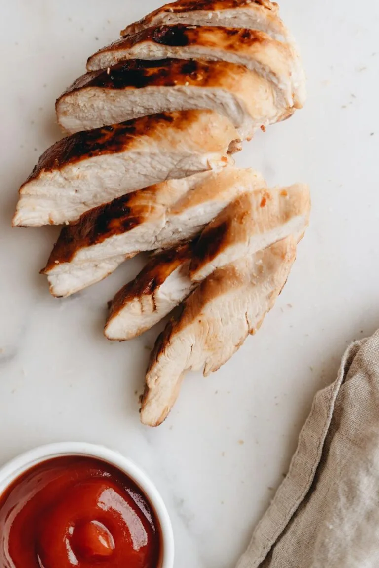 Sliced grilled chicken breast arranged on a white surface with a small bowl of sauce, perfect for easy weekly meal prep.