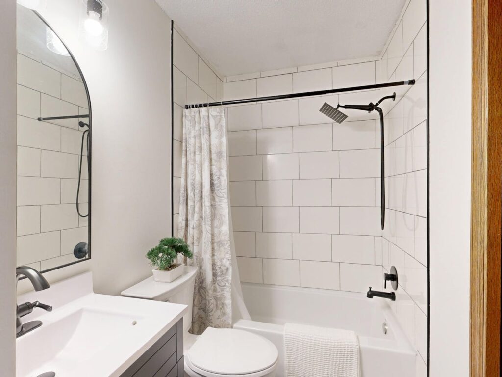 Small bathroom with white subway tile shower, modern vanity, mirror, and toilet showing practical layout and storage design.