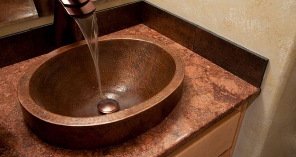 Hammered copper sink installed in a bathroom vanity with running water and warm-toned countertop
