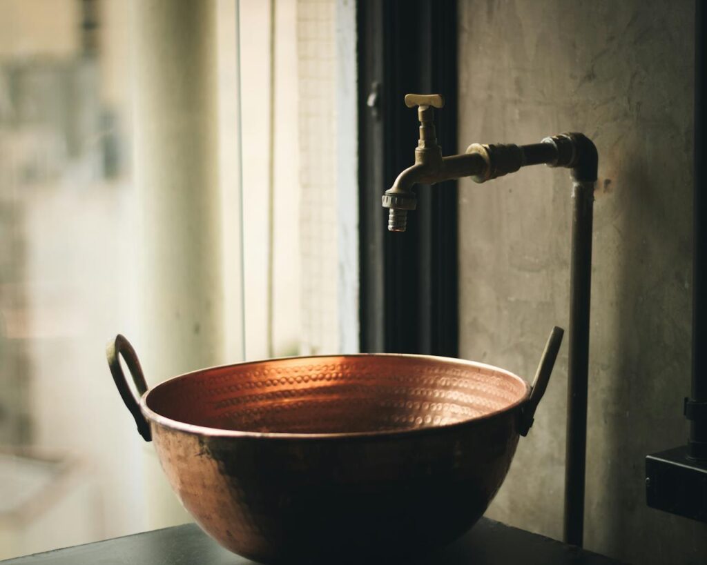Copper sink benefits shown in a rustic bathroom with a hammered copper basin and vintage faucet