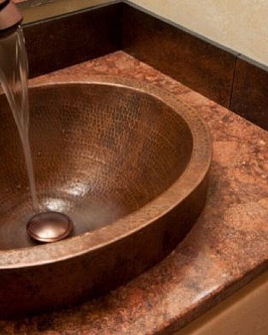 Hammered copper sink installed in a bathroom vanity with running water and warm-toned countertop