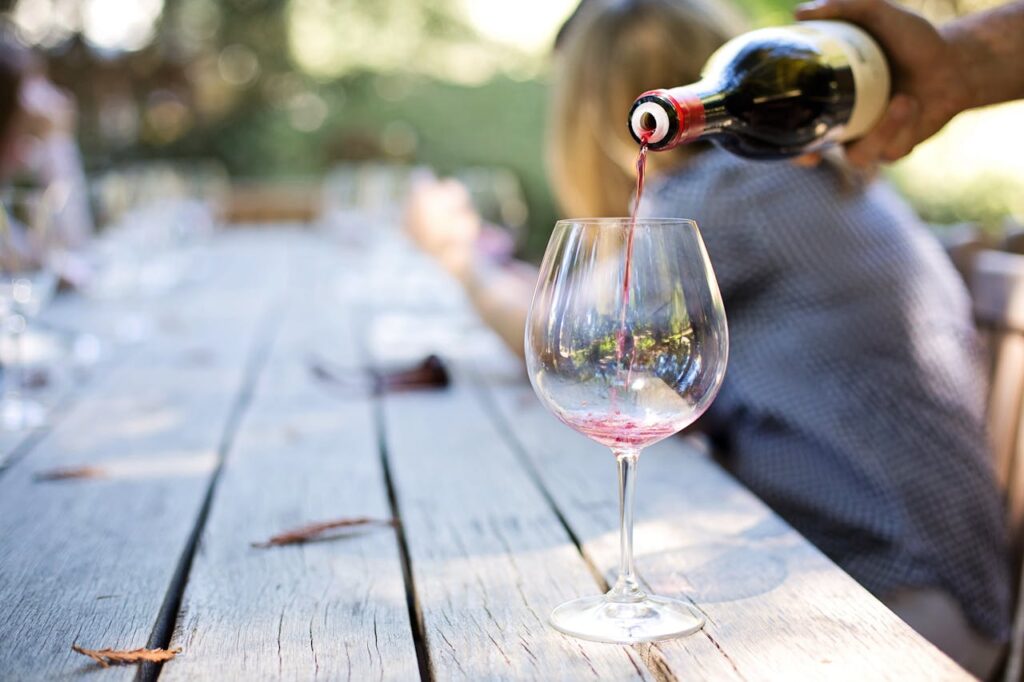 Red wine being poured into a glass during an outdoor wine tasting experience at a long wooden table