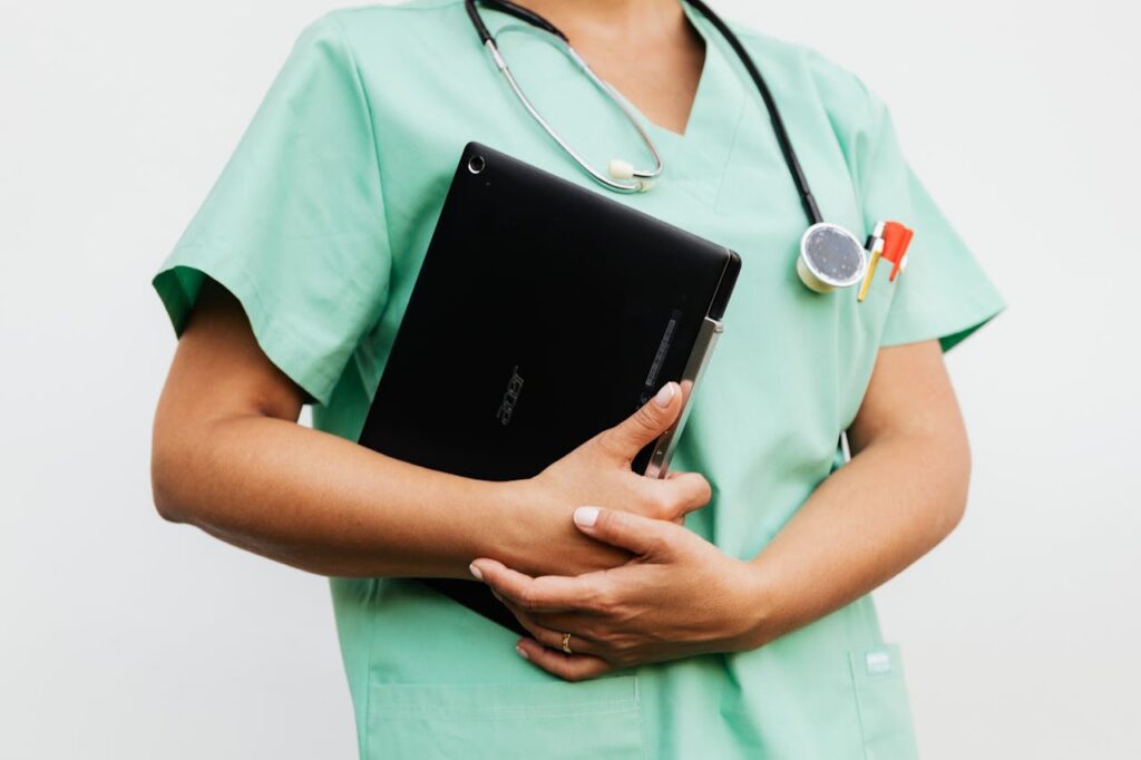 nurse practitioner in green scrubs holding a tablet with stethoscope, representing modern patient care and healthcare support