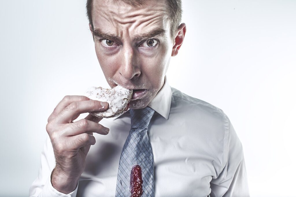 Man eating a powdered donut with food stains on his shirt, representing binge eating behavior linked to eating disorders.