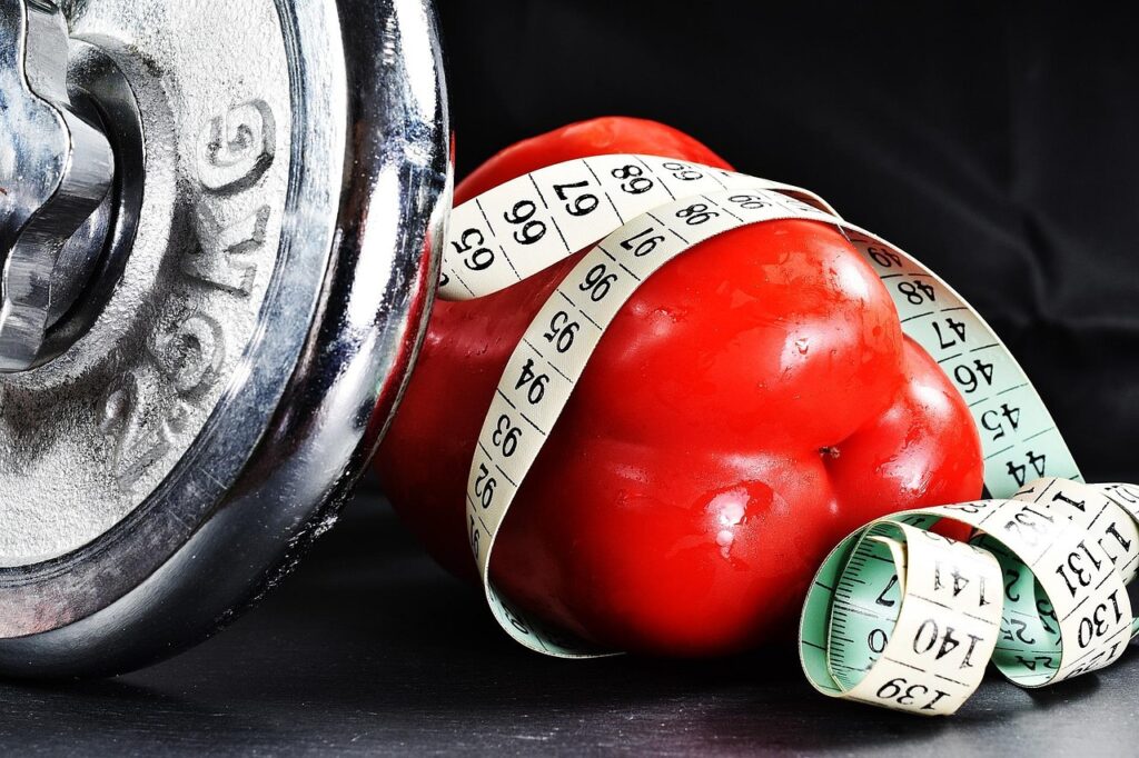 Measuring tape wrapped around a red bell pepper beside a dumbbell, symbolizing dieting culture and the signs and symptoms of an eating disorder.
