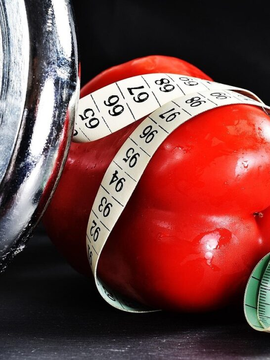Measuring tape wrapped around a red bell pepper beside a dumbbell, symbolizing dieting culture and the signs and symptoms of an eating disorder.