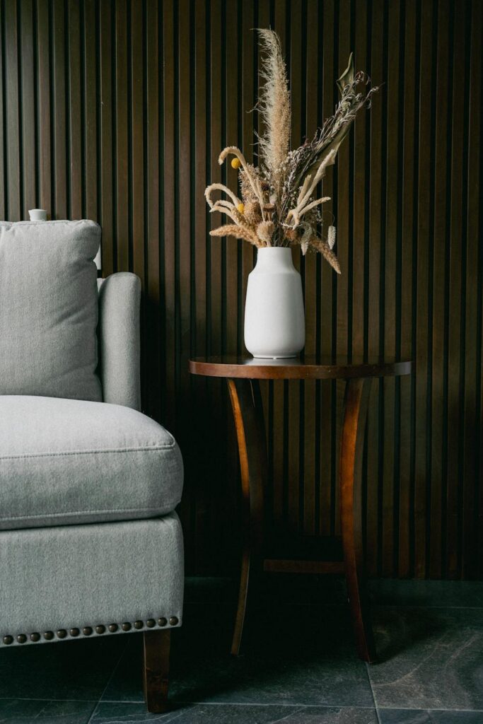 Decorative vase with dried flowers on a side table against a dark wood slat textured wall