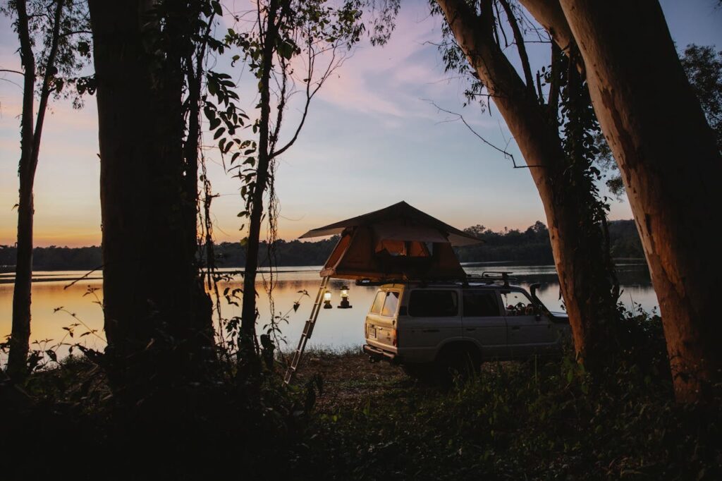 Vehicle with rooftop tent at sunset by the water surrounded by trees during an outdoor camping trip