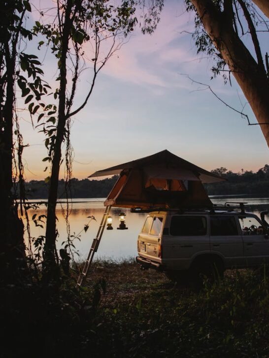 Vehicle with rooftop tent at sunset by the water surrounded by trees during an outdoor camping trip