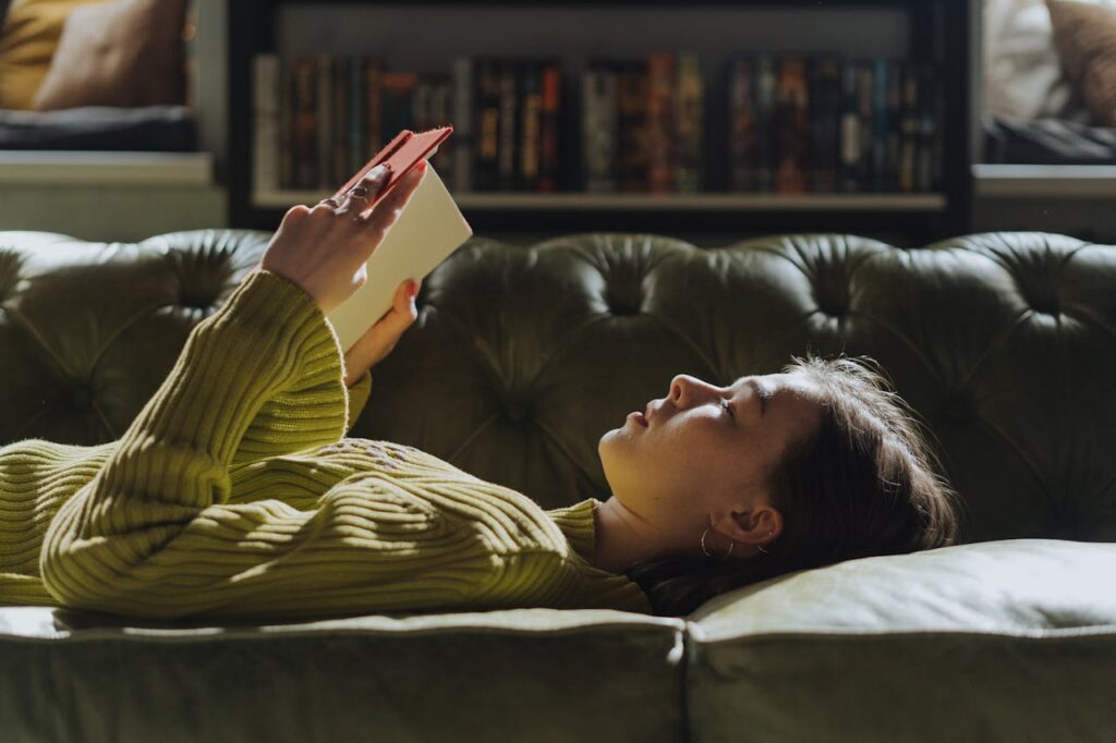 Woman relaxing on a couch reading a book, representing feminine comfort habits and daily self-care
