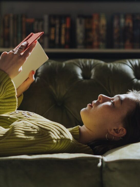 Woman relaxing on a couch reading a book, representing feminine comfort habits and daily self-care