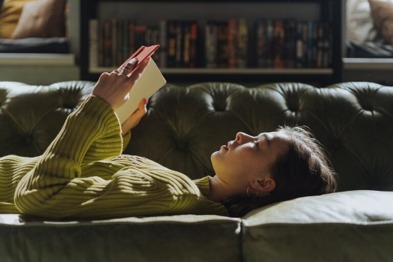 Woman relaxing on a couch reading a book, representing feminine comfort habits and daily self-care