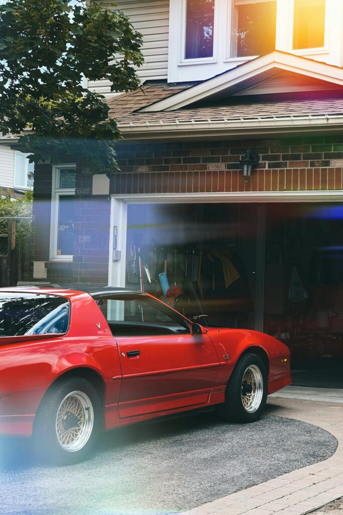 Red car parked in front of a residential garage with storage visible inside