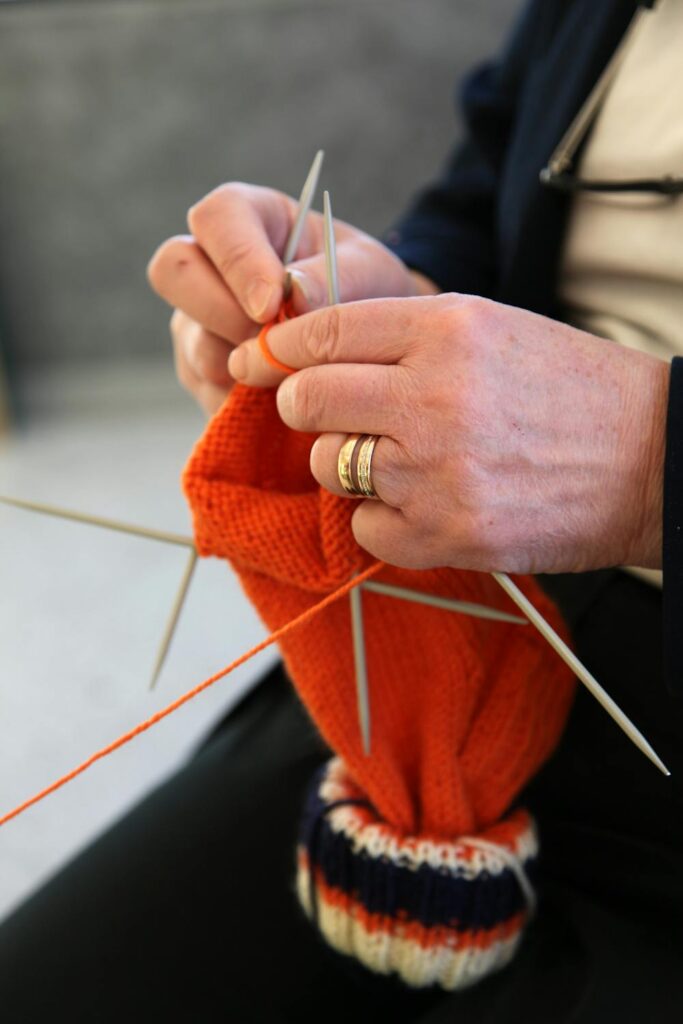 Gifts for knitters idea with hands knitting a bright orange project using double pointed needles