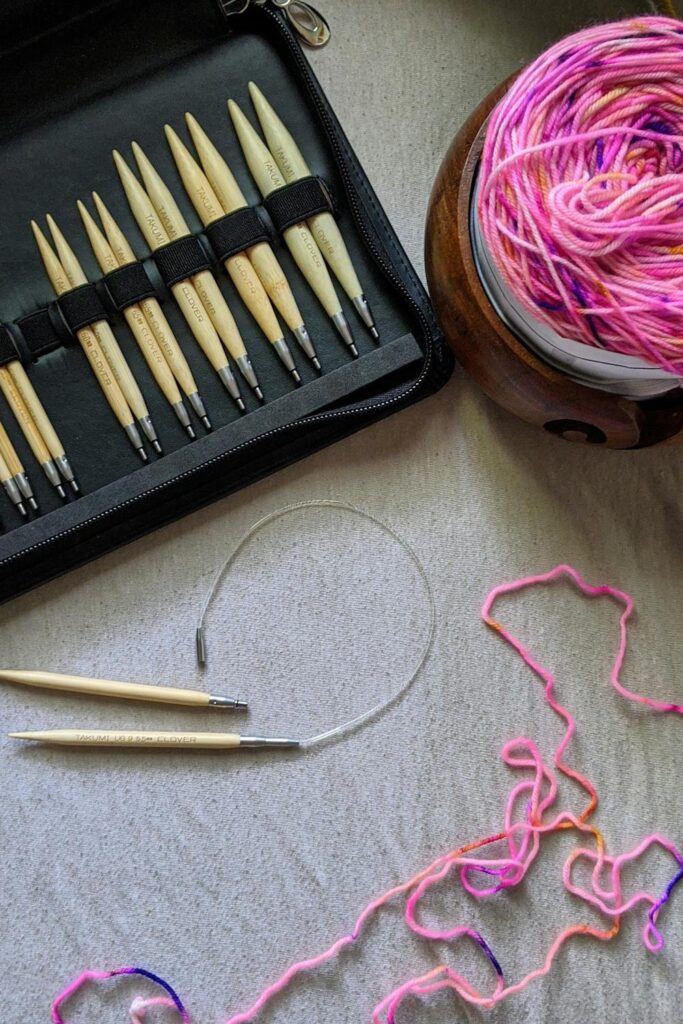 Knitting tools set with interchangeable needles, yarn bowl, and colorful yarn on fabric surface